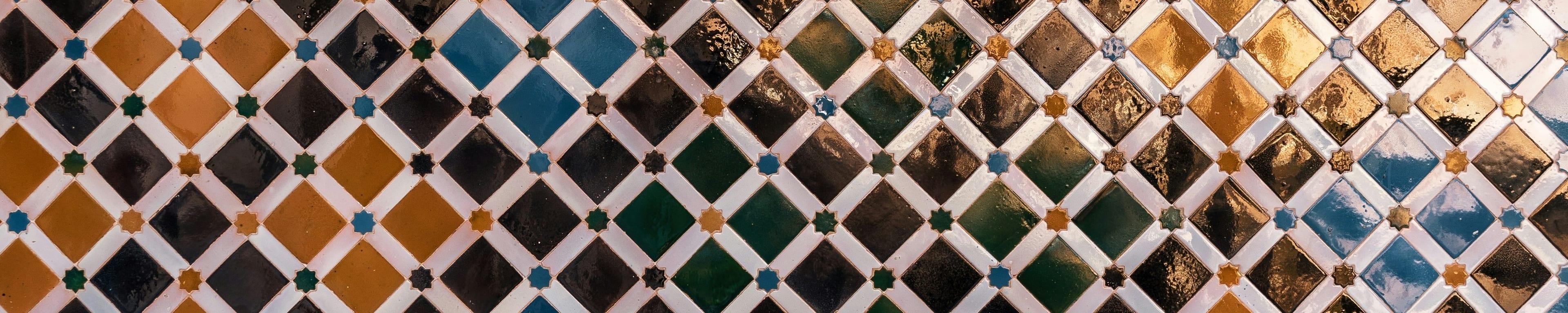 A course of hand-cut Nasrid zellij in the Alhambra: a diamond lattice of glazed tile in turquoise, deep green and gold, each cell bordered in white.